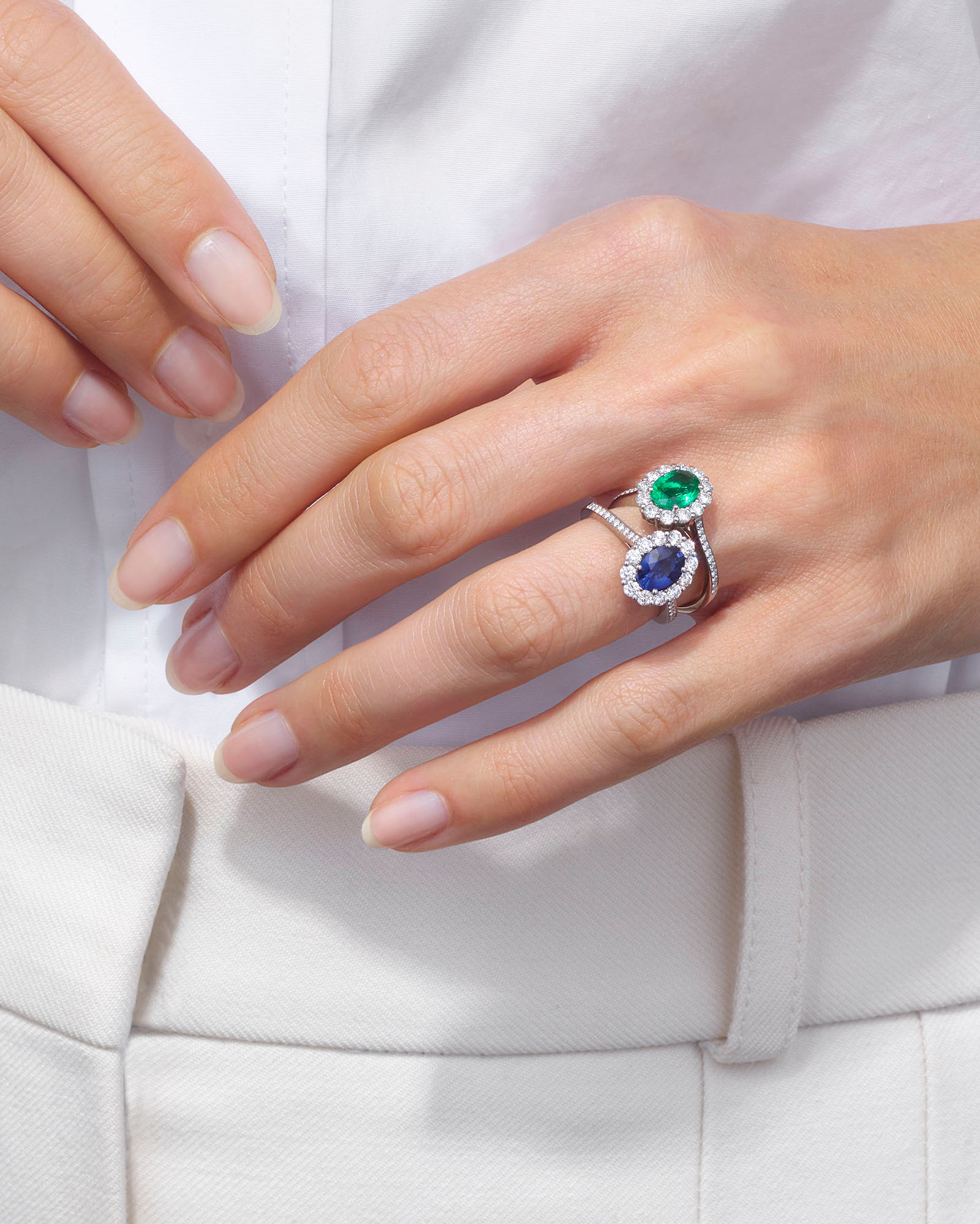 a woman wearing a stacked Garrard sapphire 1735 ring and an emerald 1735 ring on her left wedding finger close up 1