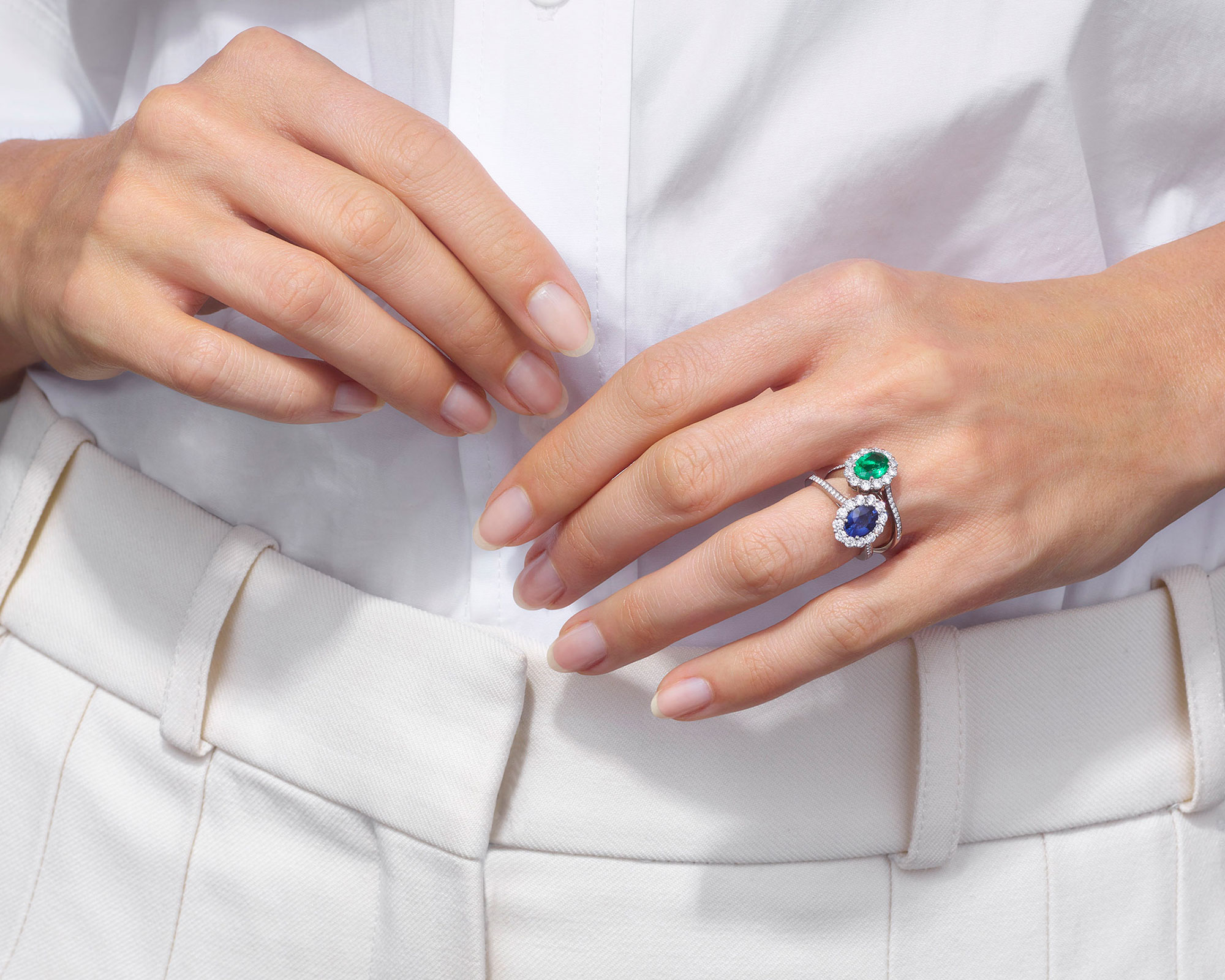 a woman wearing a stacked Garrard sapphire 1735 ring and an emerald 1735 ring on her left wedding finger mobile