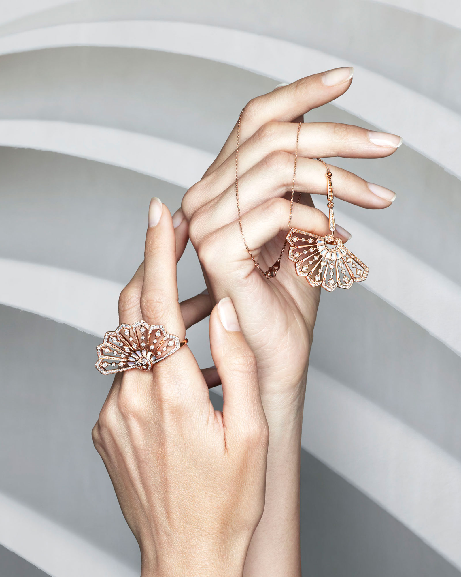 close up of a models hand holding the Fanfare jewellery collection diamond pendant and rings set in rose gold vertical
