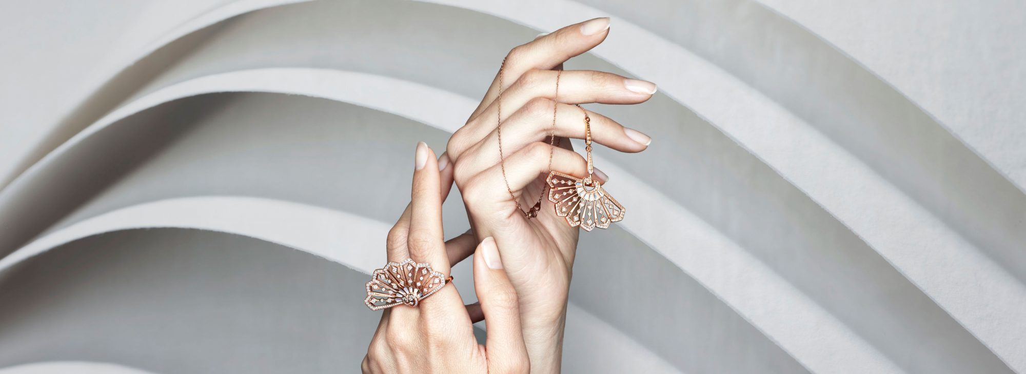 close up of a models hand holding the Fanfare jewellery collection diamond pendant and rings set in rose gold